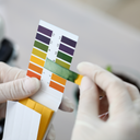 Una persona sostiene una tira de prueba con una variedad de colores para medir el pH de la piel y los cosméticos.