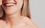 Mujer sonriendo con piel radiante y dientes blancos en un fondo neutro
